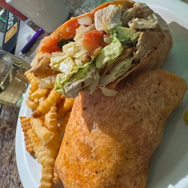 A chicken wrap with lettuce and tomatoes, served with crinkle-cut fries on a white plate.
