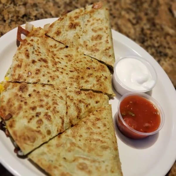 A quesadilla cut into four triangles, served with small cups of salsa and sour cream.