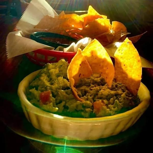 A bowl of guacamole with tortilla chips and a basket of chips and salsa in the background.