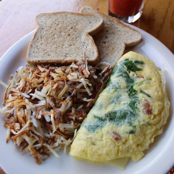 A breakfast plate with a spinach and bacon omelet, hash browns, and two slices of wheat toast.