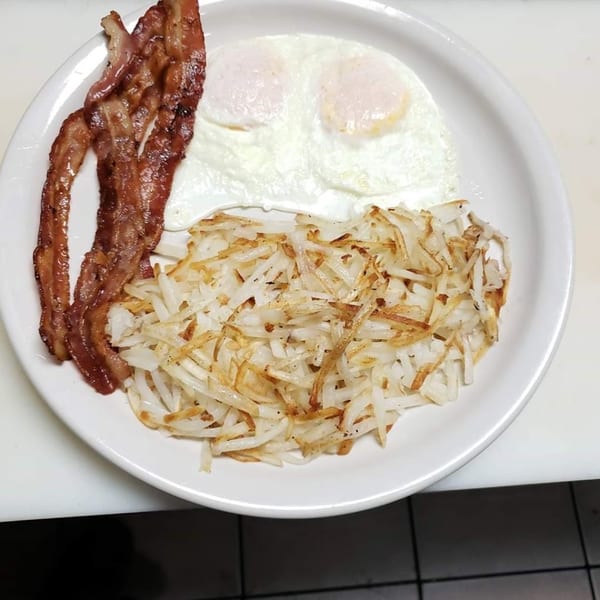 A breakfast plate with crispy bacon, two fried eggs, and golden hash browns.