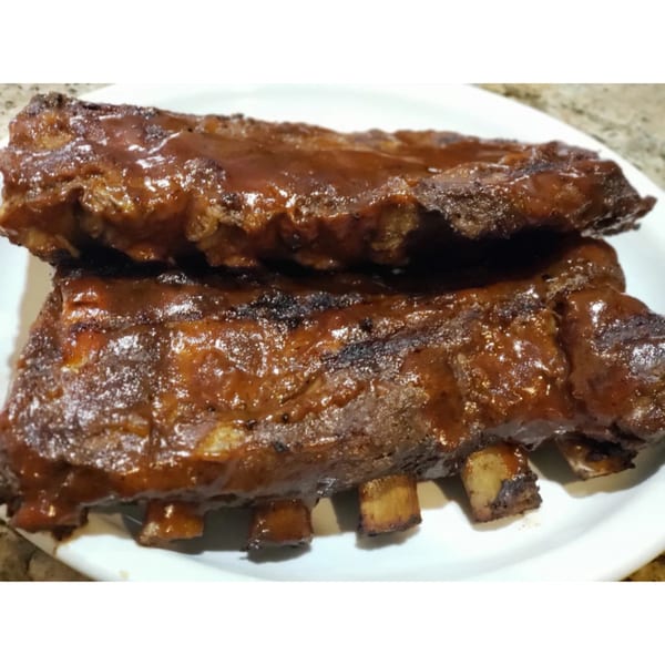 Two racks of glistening BBQ ribs, coated in a rich, dark sauce, on a white plate.