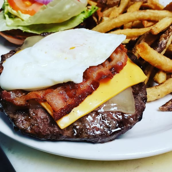 A Gio's Bar & Grill burger with bacon, cheese, and a fried egg, served with fries.